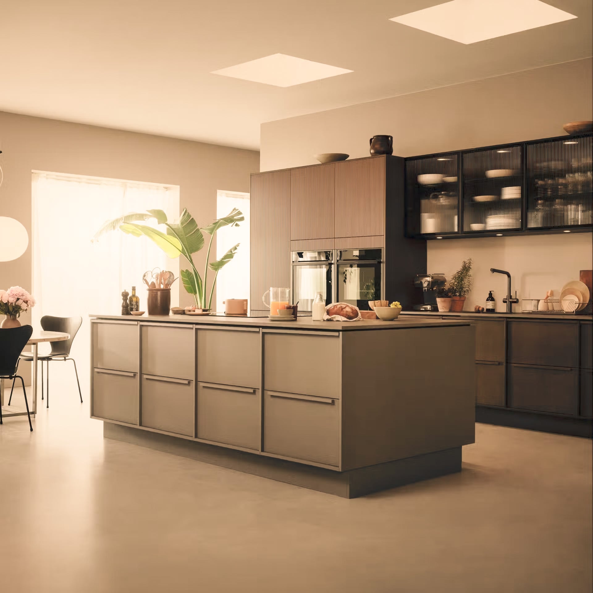 Modern kitchen with beige and black cabinets, built-in ovens, green plants, and natural light from windows
